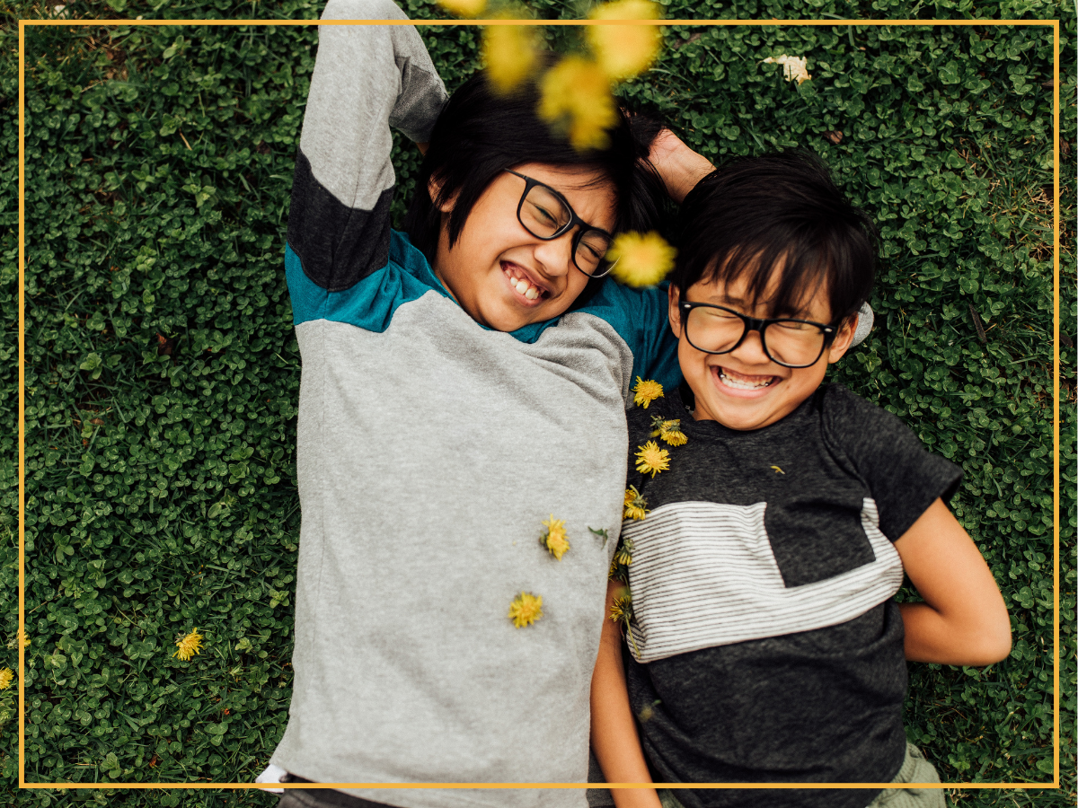 Two children with glasses lay smiling in a clover yard